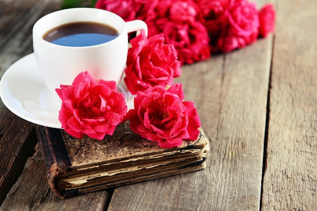 美しいバラと木製のテーブルの上のコーヒー カップの古い本をクローズ アップ