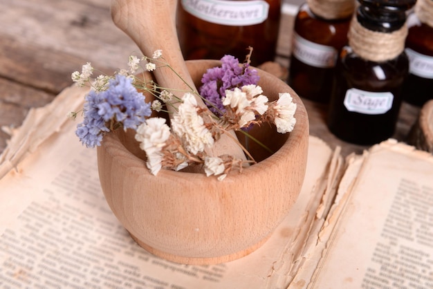 Old book with dry flowers in mortar and bottles on table close up