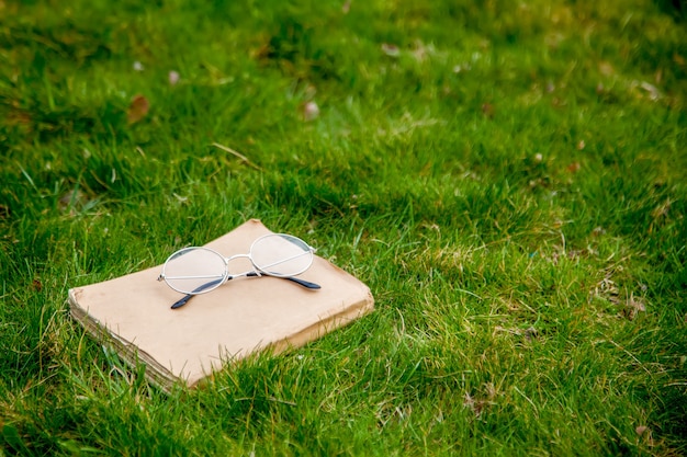 Old book with glasses for reading on green grass