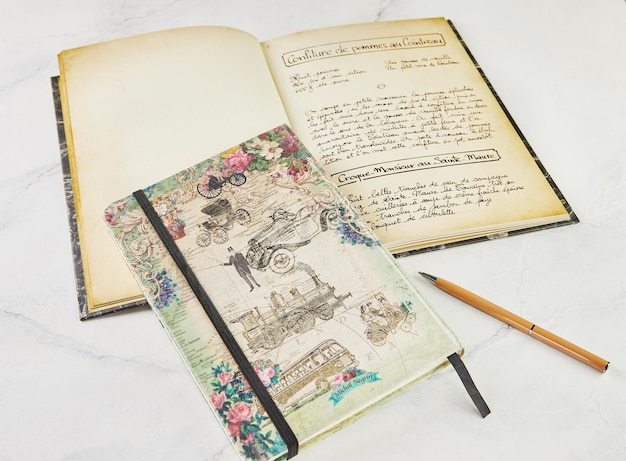 Старая книга с рецептами на французском языке и блокнот для письма ручкой на белом мраморе
