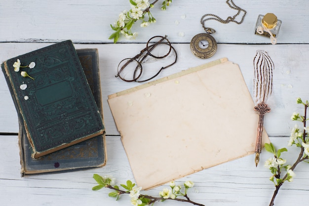 old books, empty sheets of paper, fountain pen, glasses, pocket watches and branches of blossoming cherry