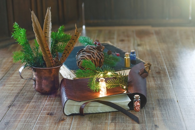 Old books with miniature flashlight and twigs of spruce lie on a wooden table close up