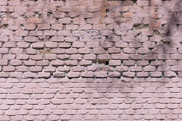 An old brick wall with deformities painted in a pale pink color