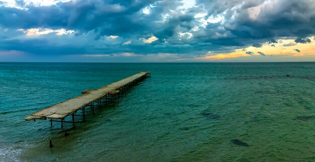 Old broken bridge in the sea at cloudy sunset panoramic view