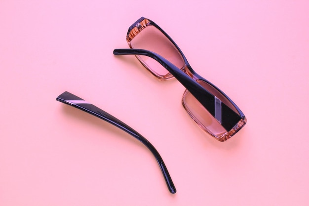 Old broken eyeglasses with damaged legs on pink background Poor eyesight Reuse and repair concept