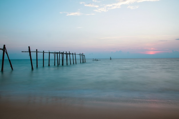 Old broken pier on the beach at the sunset background.