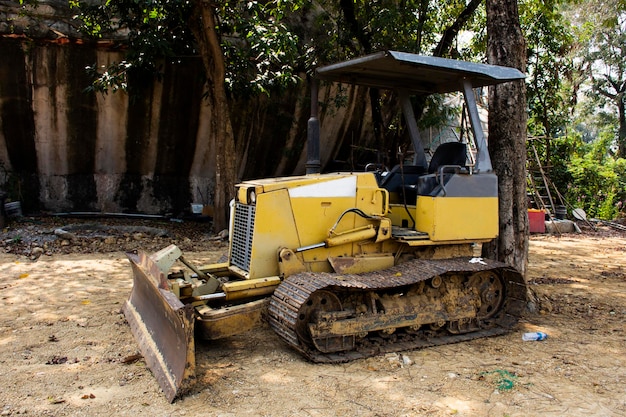 古い壊れたトラクターの機械は、タイの技術者がナコンパトムタイのサムプラン市にあるワットサンフラン寺院の土地建設現場の公園の庭で修理と修理を待つのをやめます