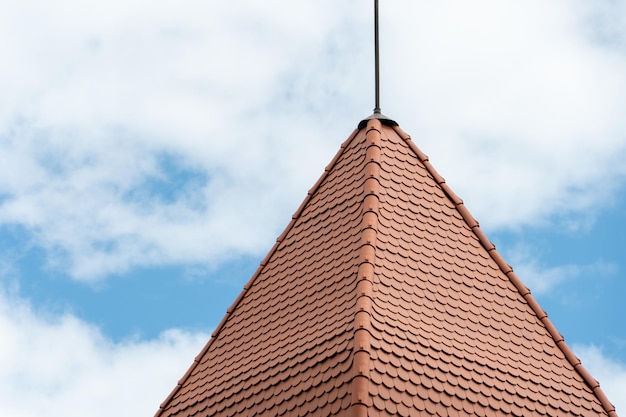 An old building with a red tiled roof on a background of blue\
sky and clouds repair and restoration of architectural monuments\
sloping tiled roof with a spire closeup