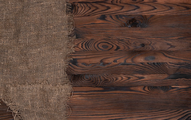 Old burlap fabric napkin on brown wooden background, top view