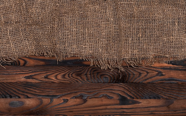 Old burlap fabric napkin on brown wooden background, top view