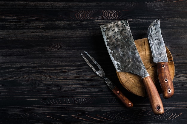 Old butcher meat knife, cleaver and fork on black