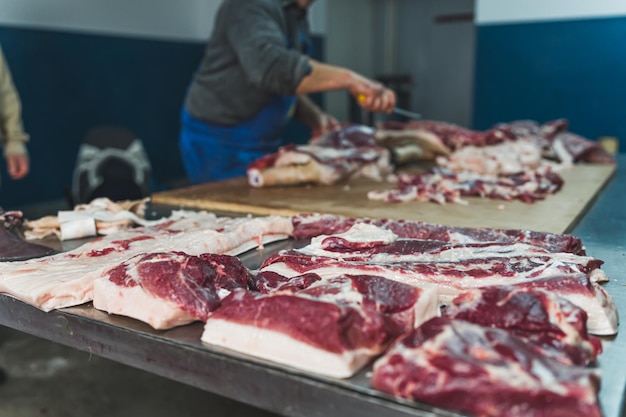 An old butcher working in the slaughterhouse cutting pork into slices