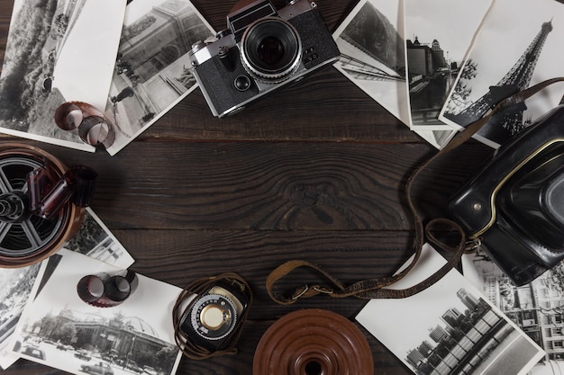 Old camera, acsessories and black and white photographs are on the dark wooden surface in retro style