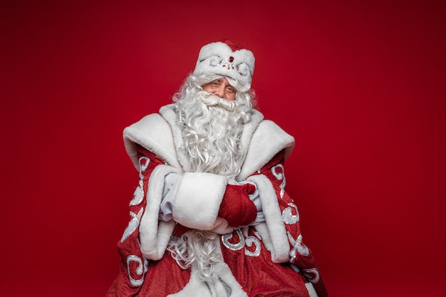 Old caucasian father frost in long warm coat, red mittens and a hat looks to the camera