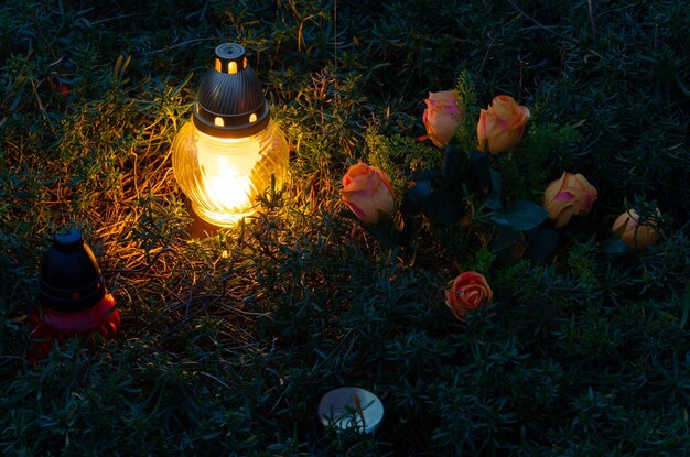 Old cemetery at night ritual lamps are lit large stone crosses\
yellow and orange flowers on graves and tombstones holiday heluen\
darkness and horror