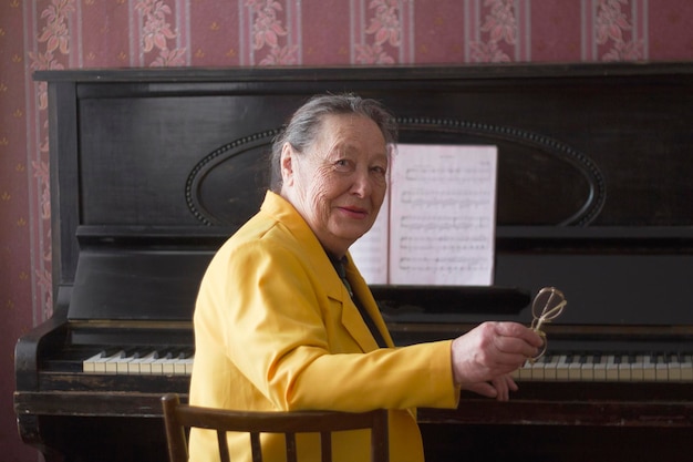 Old charming lady pianist in the yellow jacket seating at the piano, active ageing