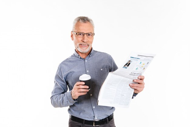 Old cheerful man holding coffee and reading newspaper isolated