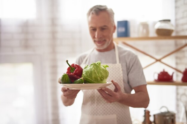 老人シェフ幸せな男皿に野菜を保持しています。