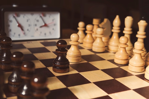 Old chess clock on the chessboard with figures ,flag in position which indicates running out of time on dark background