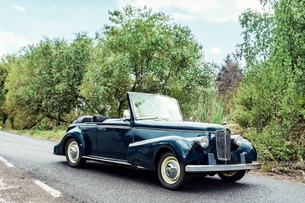 old classic black convertible car on the road with trees