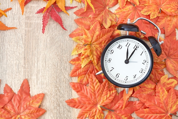 Old clock on autumn leaves on wooden table on natural background