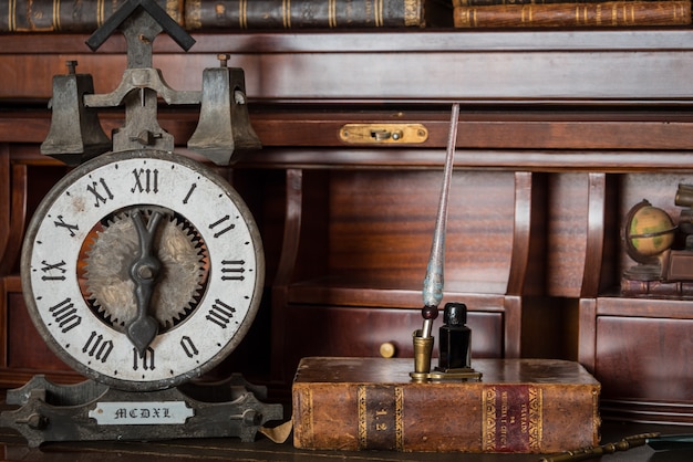 Old clock on shelf with old books and pen