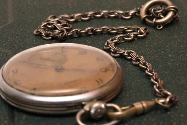 Old clock with chain lying on rough green surface