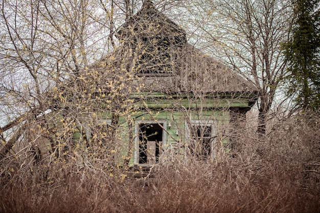 写真 秋の木の後ろに腐った漏れ屋根のある古い崩壊した放棄された家