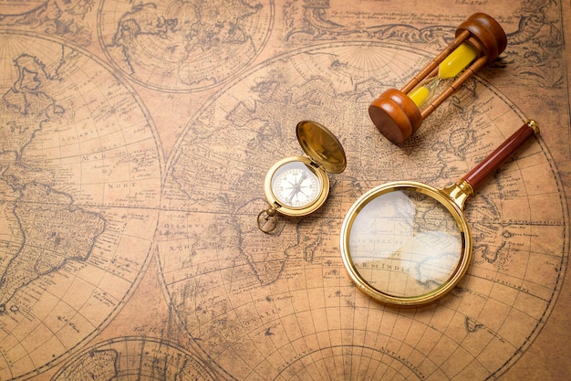 Photo old compass , magnifying glass and sand clock on vintage map