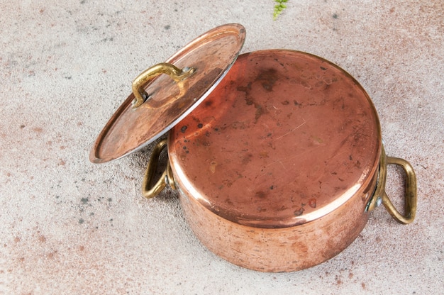 Old copper casserole with lid and brass handles on a concrete table.