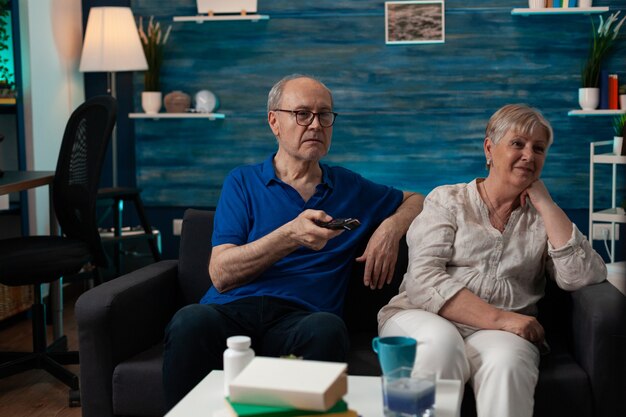 Old couple enjoying retirement at home sitting on sofa