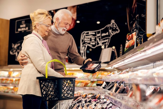 An old couple is buying fresh packed meat at butchery in supermarket