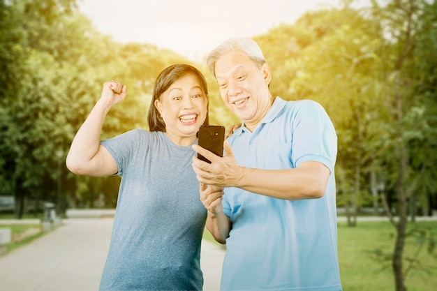 Old couple reading good news on cellphone at park