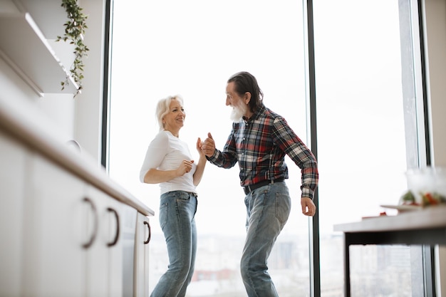 Photo old couple spends free time dancing twist in modern light kitchen