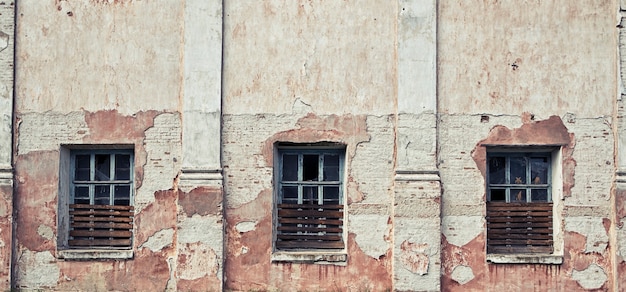 The old and damaged abandoned wall with windows with broken glass