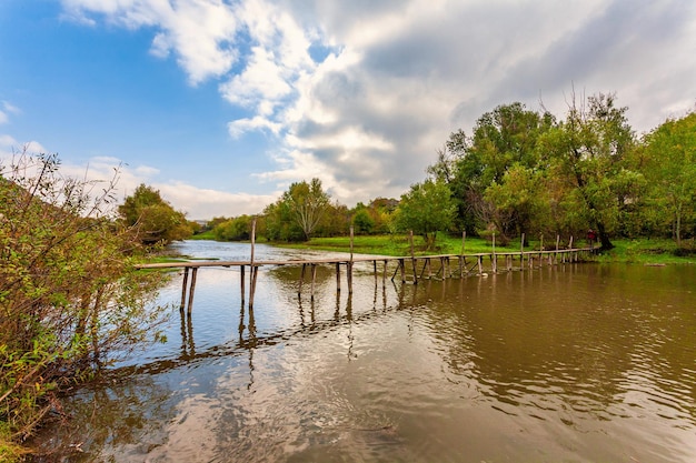 Old and damaged rope and wooden boards bridge over the small river