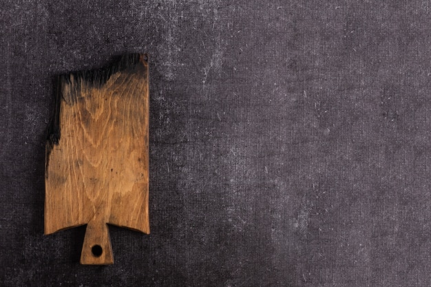 An old dark cutting board on a dark background. The board is charred