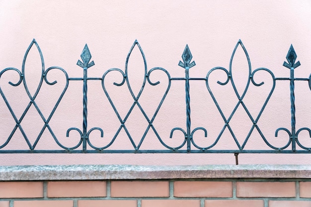 Photo old decorative wrought-iron fence on a brick foundation against the background of a plastered pink wall