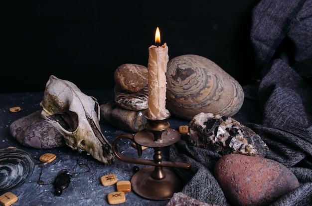 Фото Старый собачий череп, горящая свеча, деревянные руны и камни на волшебном столе.