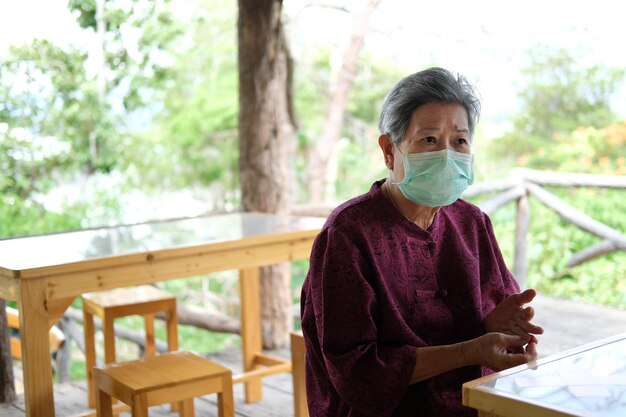 Фото Пожилая женщина в медицинской маске на лице отдыхает в саду азиатский пожилой пожилой расслабляется