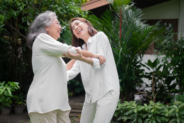 An old elderly Asian woman and dance in the backyard with her daughter