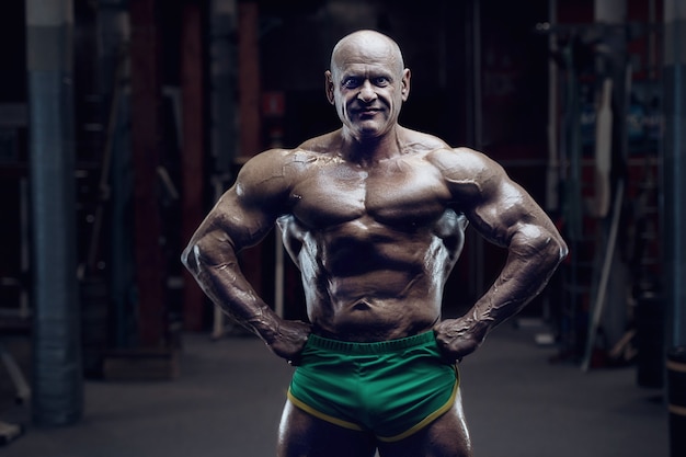 Old fashion athlete bodybuilder doing arm exercises in gym. Brutal bald caucasian sports man style of the 80s. Sport, fitness and workout 80s concept