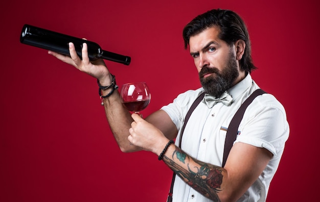 Old fashioned bearded hipster winemaker trendy man in\
suspenders and bow tie with wine confident elegant man drinking\
wine from glass alcoholic drink stylish sommelier tasting\
beverage