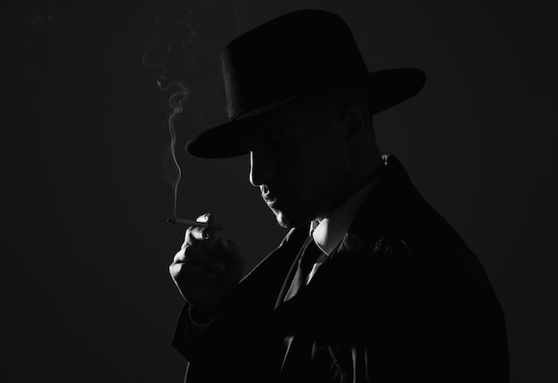 Old fashioned detective smoking cigarette on dark background black and white effect