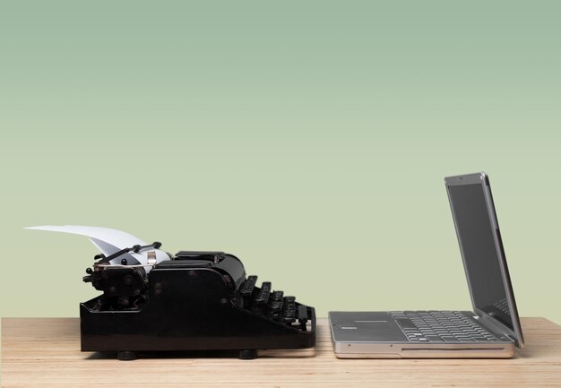 Old fashioned typewriter with a modern laptop computer on wood desk