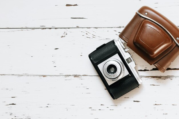 Old film camera in brown vintage case and a roll of film on wood background top view text spacex9