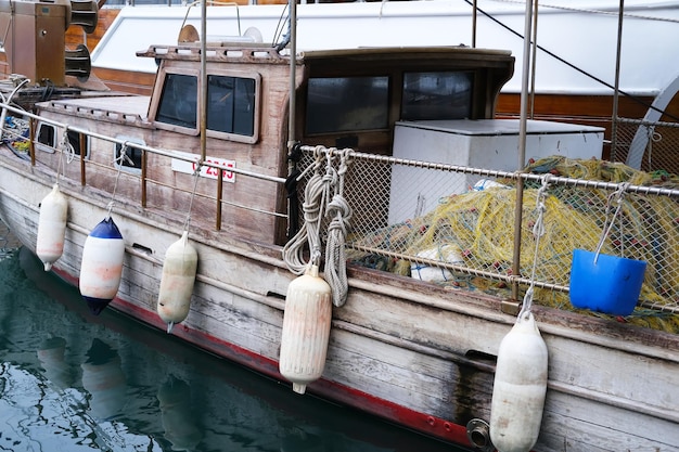 Old fishing boat with fishing nets and boat fenders balls in\
the harbor