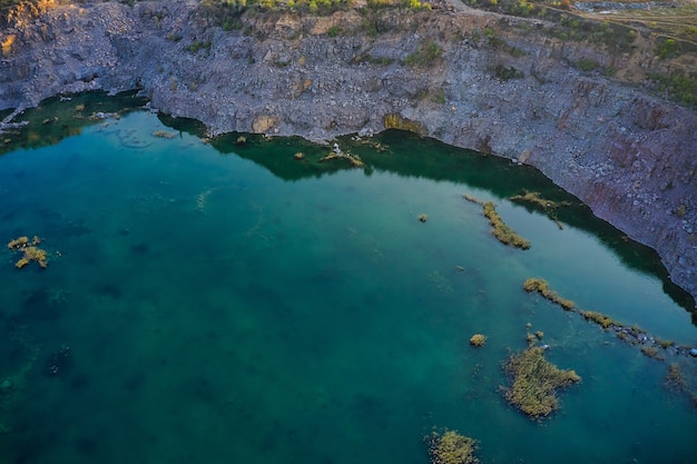 Old flooded stone quarry with large stones in the evening warm bright light covered with small dry plants in picturesque Ukraine. Aerial panoramic drone shot