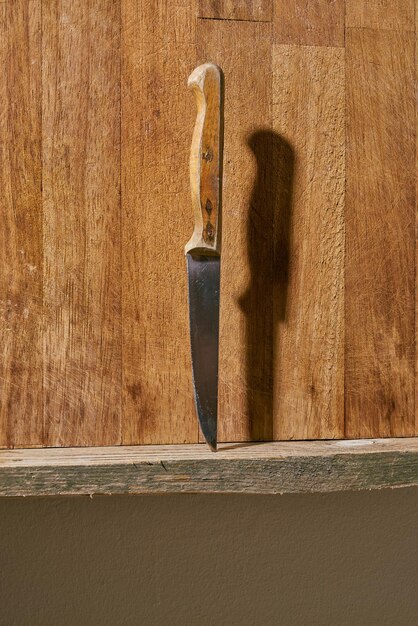 Old fruit knife with wooden handle stabbed on a wooden kitchen shelf.