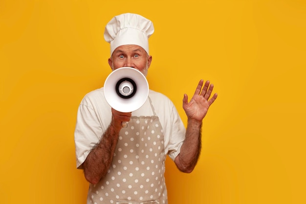 Old grandfather chef in apron and hat announces information into megaphone